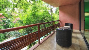 A balcony with a wooden railing, wicker furniture, and a view of lush greenery. - Mi Querido Tulum Apt with Pool-View (Tulum)