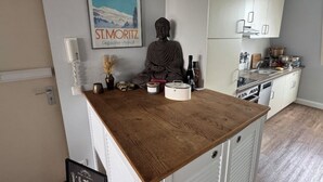 Keittiössä on valkoiset kaapit, puinen työtaso ja Buddha-patsas.