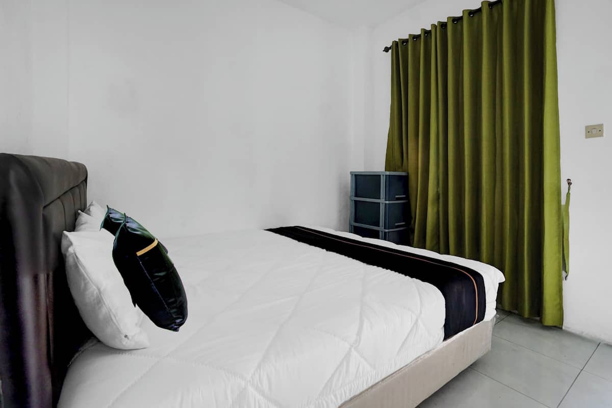 Uma cama de solteiro com colchão branco acolchoado, cabeceira escura e duas almofadas. Uma unidade de armazenamento azul está encostada na parede.