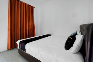 A neatly made bed with white bedding and a dark headboard, a brown bedside table, and orange curtains on a white wall. - Hotel O near Jatim Park 3 formerly Srikandi Residence (Batu)