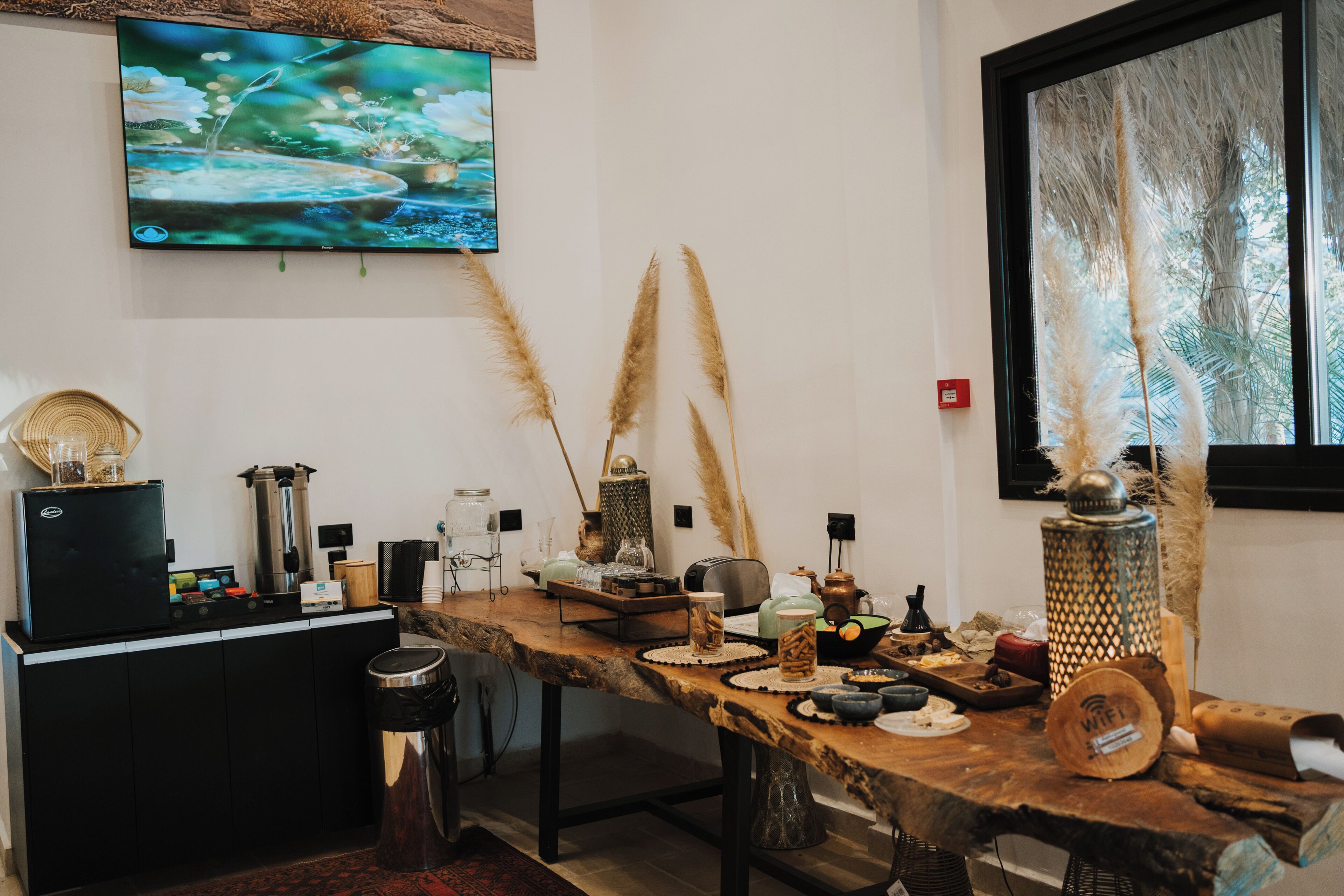 A kitchen with a wooden table, a TV mounted on the wall, and various kitchen appliances.