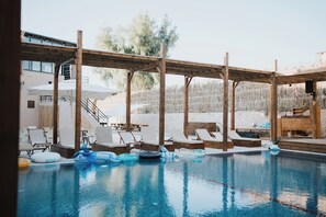 A pool area with lounge chairs, a wooden pergola, and a view of the surrounding landscape.