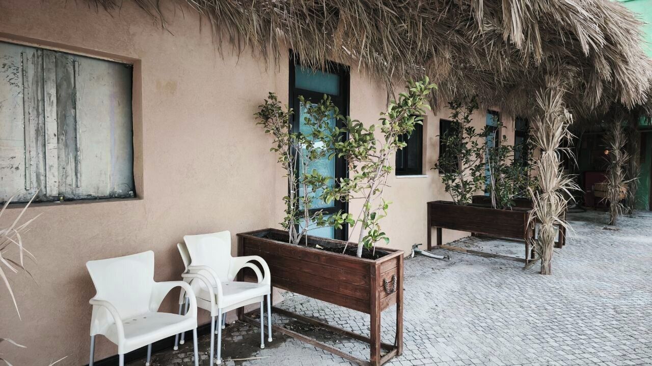 A courtyard with a thatched roof, white plastic chairs, and wooden benches.