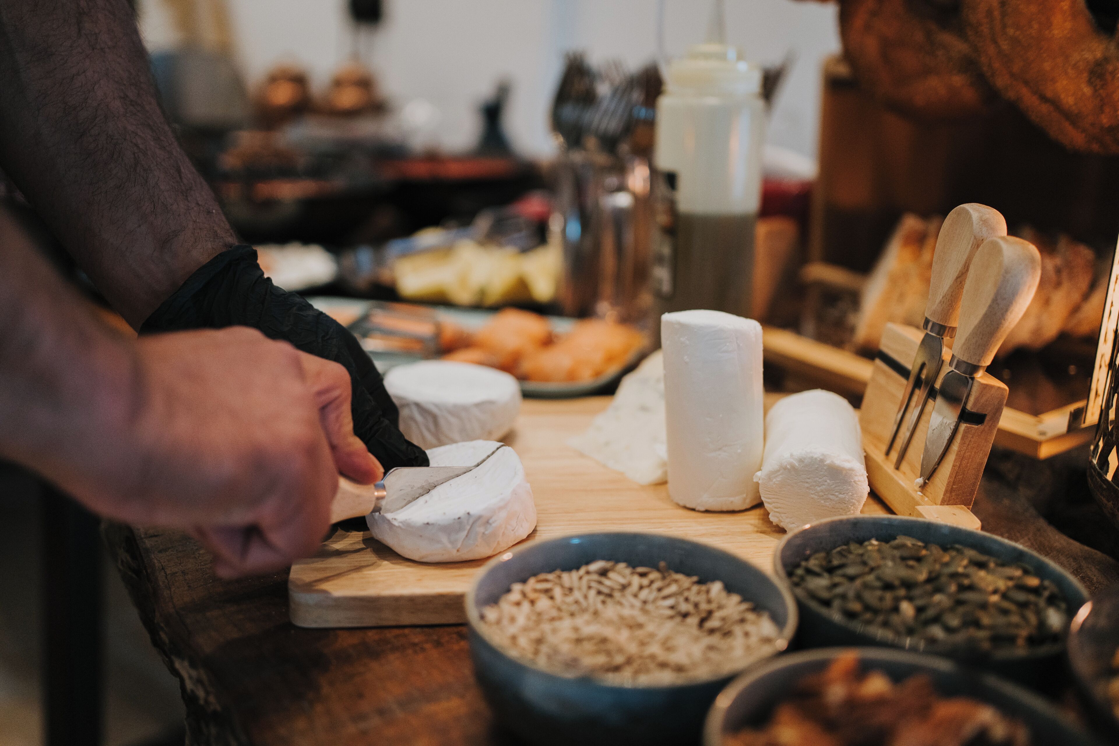 A person cutting a wheel of cheese on a wooden cutting board.