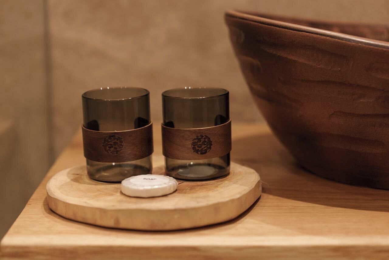 Two glass candle holders on a wooden tray with a soap dispenser.