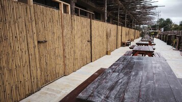 Una cerca de bambú, bancos de madera al aire libre y un corredor cubierto.