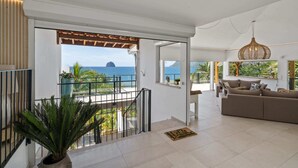 Ein geräumiger Wohnbereich mit Balkon und Meerblick, modernes Interieur und ein großes Fenster mit Blick auf den Ozean.