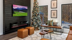 Uma sala de estar moderna com lareira, uma árvore de Natal grande e uma televisão exibindo uma paisagem cênica.