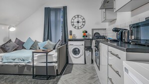 A compact living space with a sofa, a washing machine, a microwave, and a clock on the wall. - Modern 1 Bed - Near City Centre  (Manchester)