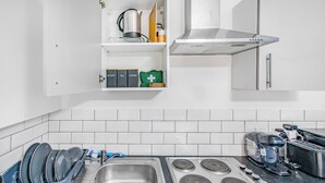 A kitchen with a stainless steel sink, four burners, a coffee maker, and a dish rack. - Modern 1 Bed - Near City Centre  (Manchester)