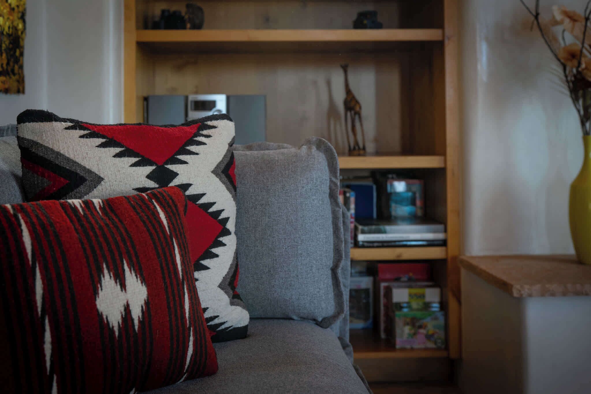 A sofa with patterned cushions and a bookshelf in the background.