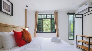 Habitación de hotel con una cama grande, cabecera de madera, ventana con cortinas y una pequeña mesa con estantes.