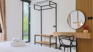 Habitación de hotel con una cama, un escritorio con silla, una ventana con cortinas, un espejo montado en la pared y una estantería con adornos.