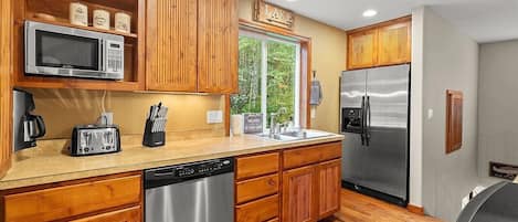 Una cocina con armarios de madera, electrodomésticos de acero inoxidable, lavavajillas y ventana con vistas a zonas verdes.