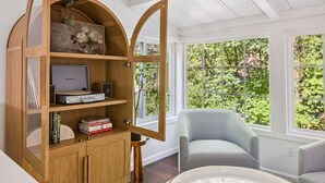 Une pièce avec une bibliothèque en bois à arc contenant des livres et des appareils électroniques, un fauteuil bleu clair et une table ronde.