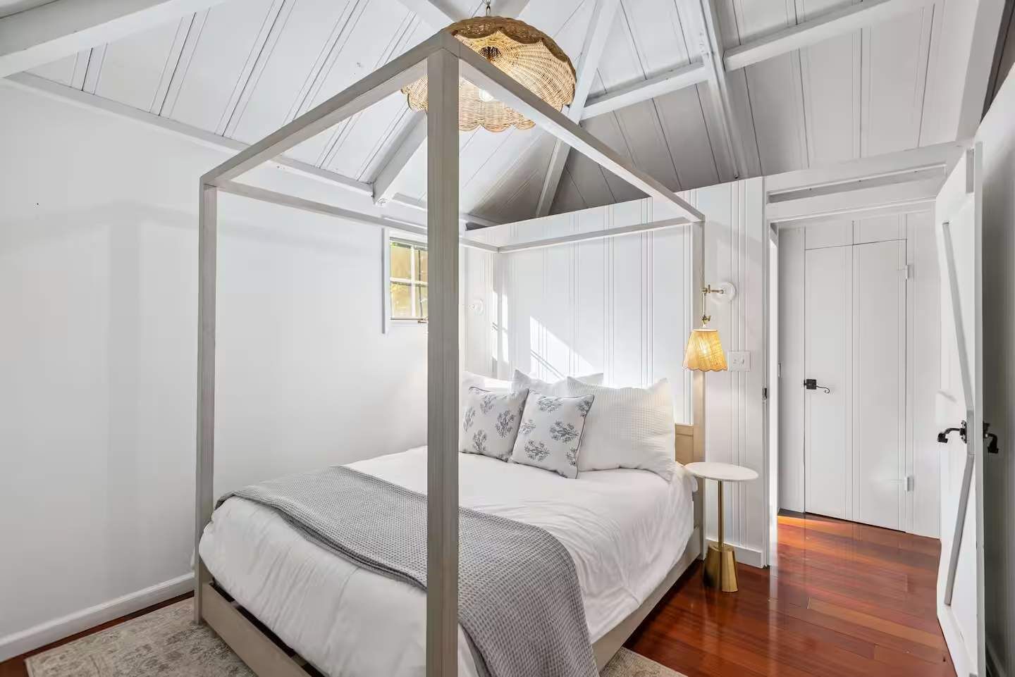 Un dormitorio con cama con dosel, una mesita de noche con lámpara y una puerta a la derecha.
