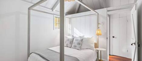 Un dormitorio con cama con dosel, una mesita de noche con lámpara y una puerta a la derecha.