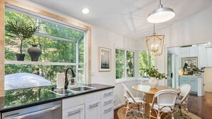Une cuisine moderne dotée d’une grande fenêtre, de meubles blancs et d’un coin repas avec des chaises en osier.