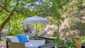 Un espace extérieur aménagé, abrité et doté d’un canapé en osier, d’une table et d’un parasol.