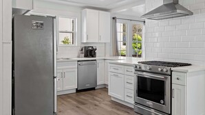 Una cucina moderna con mobili bianchi, un frigorifero in acciaio inossidabile, una lavastoviglie, un forno e un piano cottura a gas.