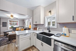 A modern kitchen with white cabinets, a black sink, and a dishwasher. There is a window with a view of the outside, and a ceiling fan above the sink. - Central Coeur d'Alene Home w/ Patio & Easy Access to Lake (Coeur d'Alene)