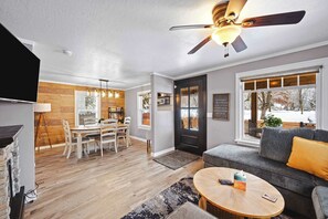 A modern living room with a wooden floor, a ceiling fan, a sofa, a coffee table, and a dining area with a table and chairs. - Central Coeur d'Alene Home w/ Patio & Easy Access to Lake (Coeur d'Alene)