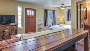 Une chambre d’hôtel avec un banc en bois, un lit, une télévision et un ventilateur de plafond.