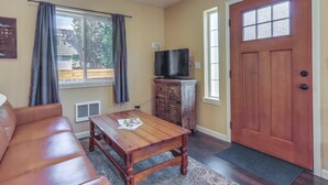 Un salon avec une table en bois, un canapé en cuir, un téléviseur posé sur un meuble et une porte en bois.