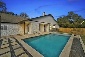 A modern house with a stone exterior, a swimming pool, and a wooden deck. - Spacious 7-Bedroom Compound w 2 Large POOLS, Fire-pit, Grill & fully-fenced yard (Austin)