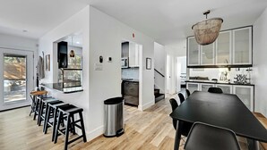 Eine moderne Küche mit Essbereich, ausgestattet mit einem langen Tisch, Barhocker und einer Pendelleuchte.
