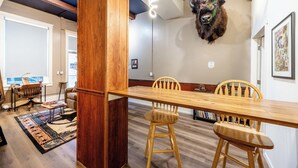 Un coin repas avec une table et des chaises en bois, une tête d’animal fixée au mur et une bibliothèque en arrière-plan.