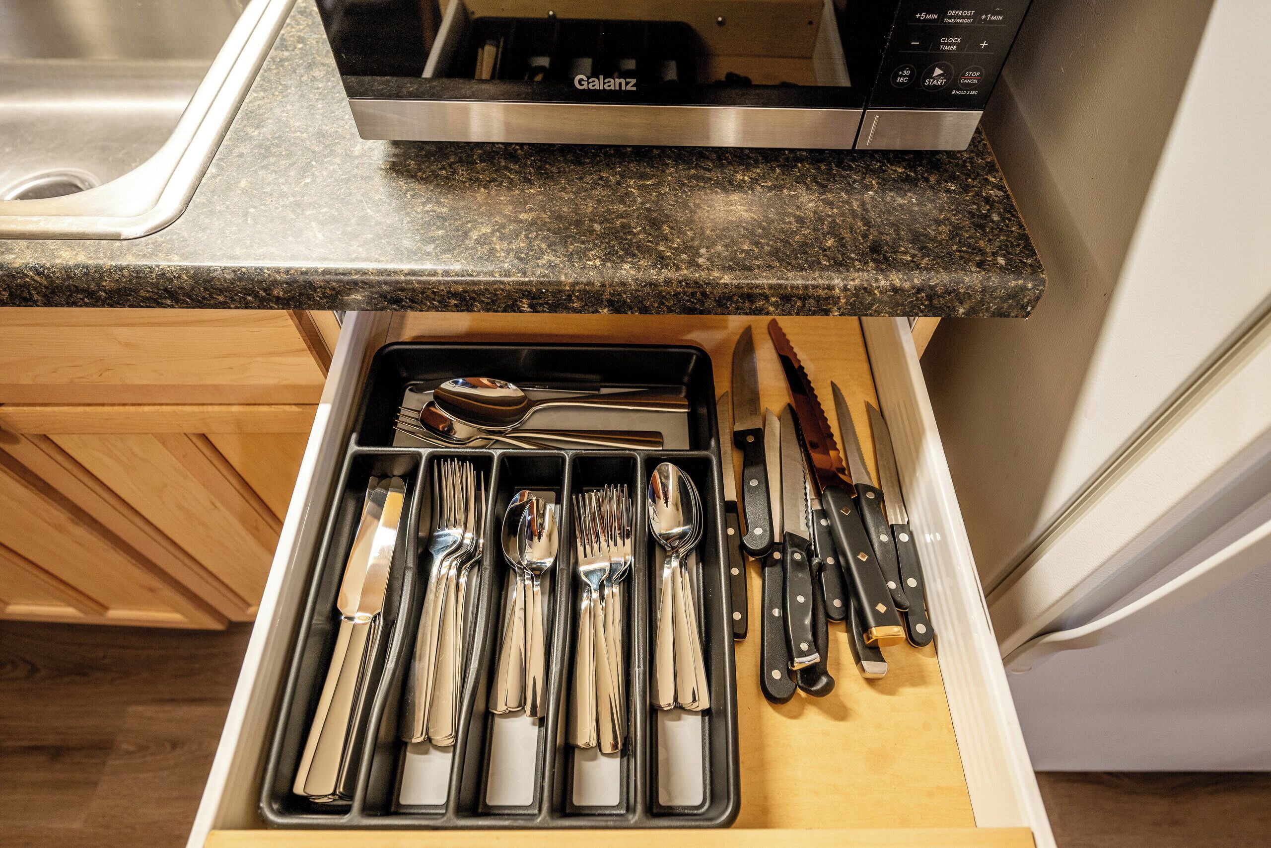 A kitchen with a granite countertop, a dishwasher, and a drawer organizer with utensils.