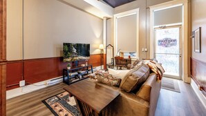 Un salon avec un plancher en bois, un canapé, une table basse, un téléviseur et une bibliothèque.