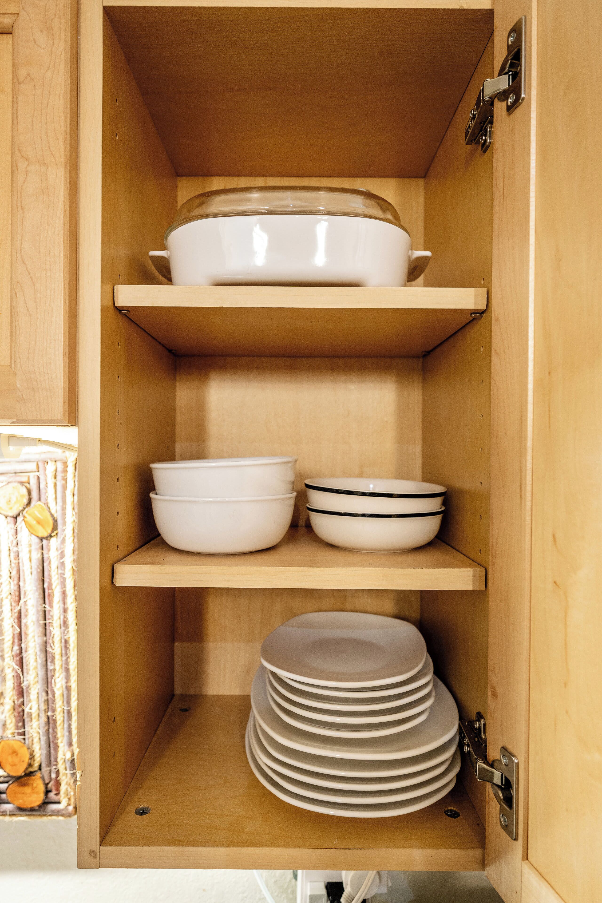 A wooden cabinet with shelves holding white bowls and plates.