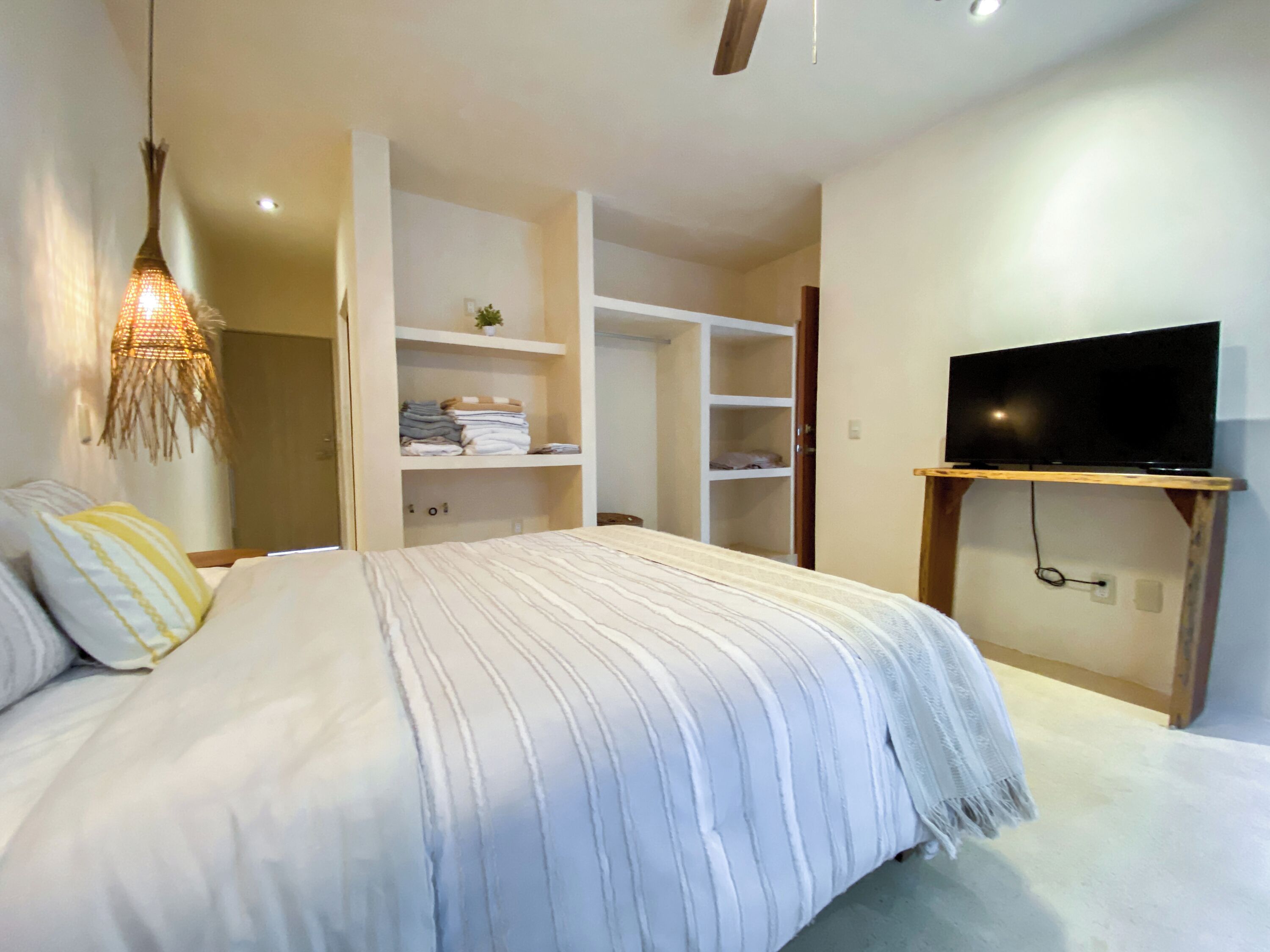A bedroom with a bed, a TV mounted on a wooden stand, a wardrobe, and a hanging light fixture.