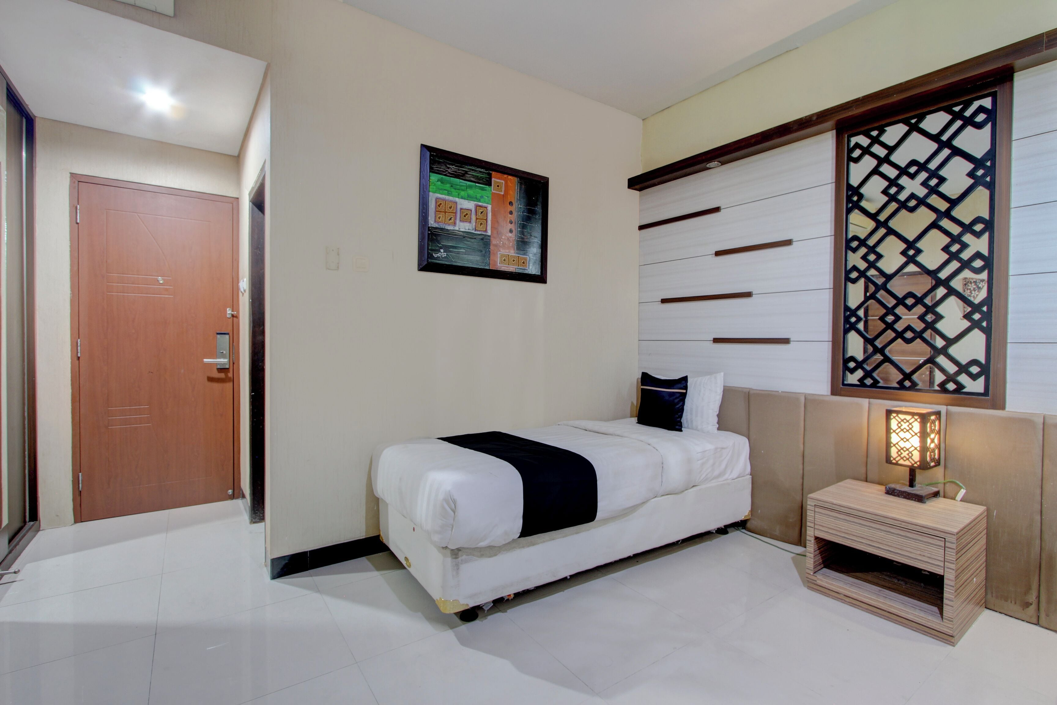 A bedroom with a bed, a nightstand, a wall-mounted artwork, and a decorative screen.