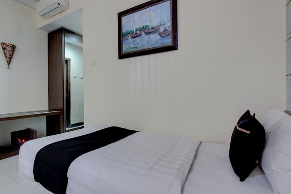 A hotel room with a bed, a painting of boats on the wall, a wooden nightstand, and a mirror. - Collection O near Stadion Manahan (Surakarta)