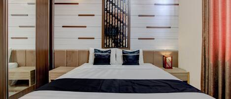 A modern hotel room with a large bed, wooden headboard, and a decorative wall panel.