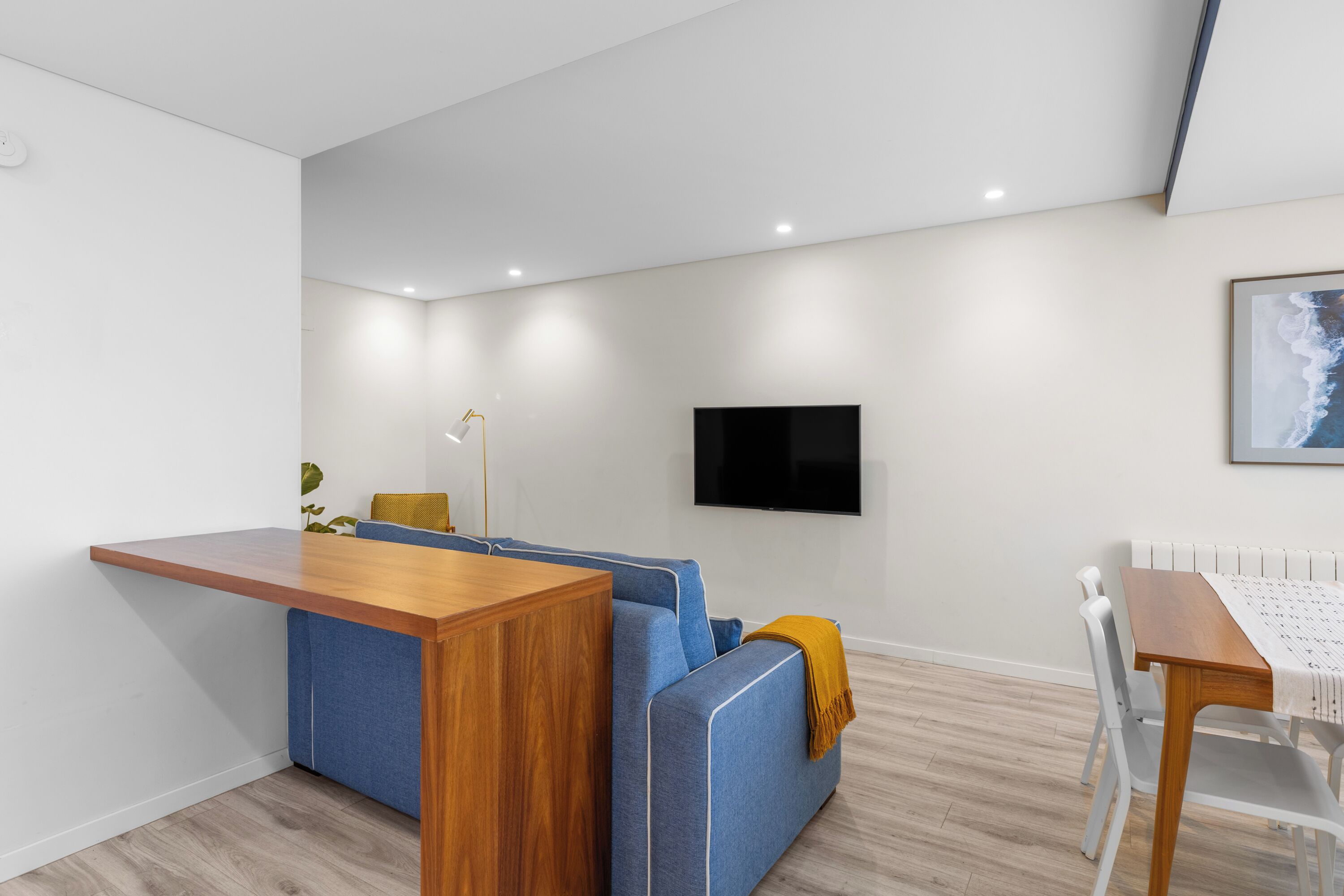 Een moderne woonkamer met een houten eettafel, een blauwe bank en een flatscreen televisie aan de muur.