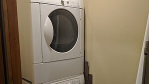 A stacked washer and dryer unit in a laundry room with a wooden door frame and a tiled floor. - Alpine Retreat - Ski & Golf Across From Hill - Full Townhouse - Fully Stocked (Ellicottville)