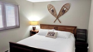 A neatly made bed with white linens and two pillows, a bedside lamp, and a wall-mounted heart-shaped decoration. - Alpine Retreat - Ski & Golf Across From Hill - Full Townhouse - Fully Stocked (Ellicottville)