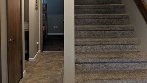 A hallway with a carpeted staircase, a wooden door, and a tiled floor. - Alpine Retreat - Ski & Golf Across From Hill - Full Townhouse - Fully Stocked (Ellicottville)