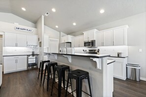 A modern kitchen with white cabinetry, stainless steel appliances, and a central island with bar stools. - Relaxing Stay Pet Friendly King Near the Lake (Nampa)