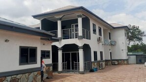 A two-story building with a balcony, a gated entrance, and a paved courtyard. - SNS Apartments (Adentan)