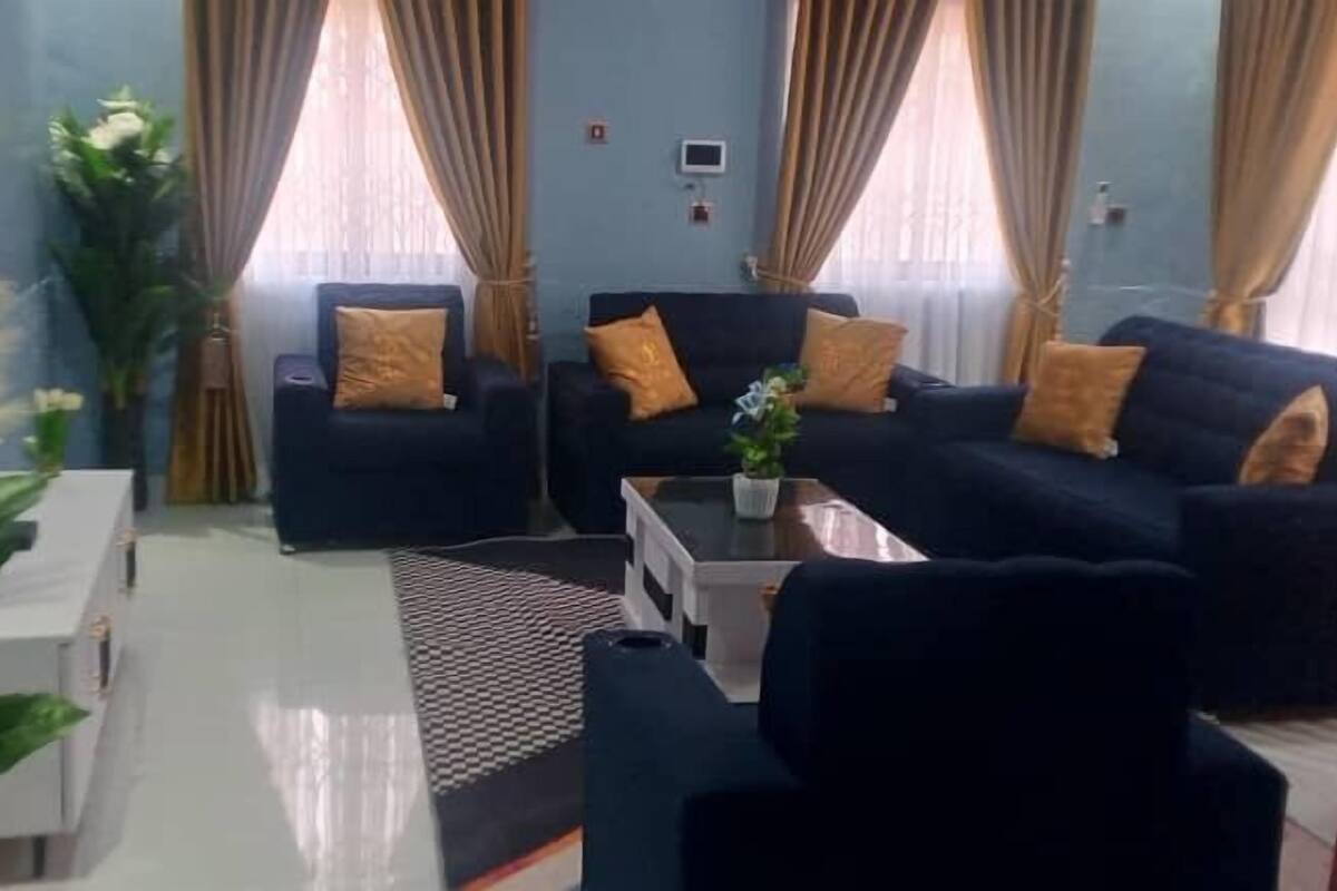 A living room with two sofas, a coffee table, and a TV. There are curtains, a plant, and a small table with a plant.