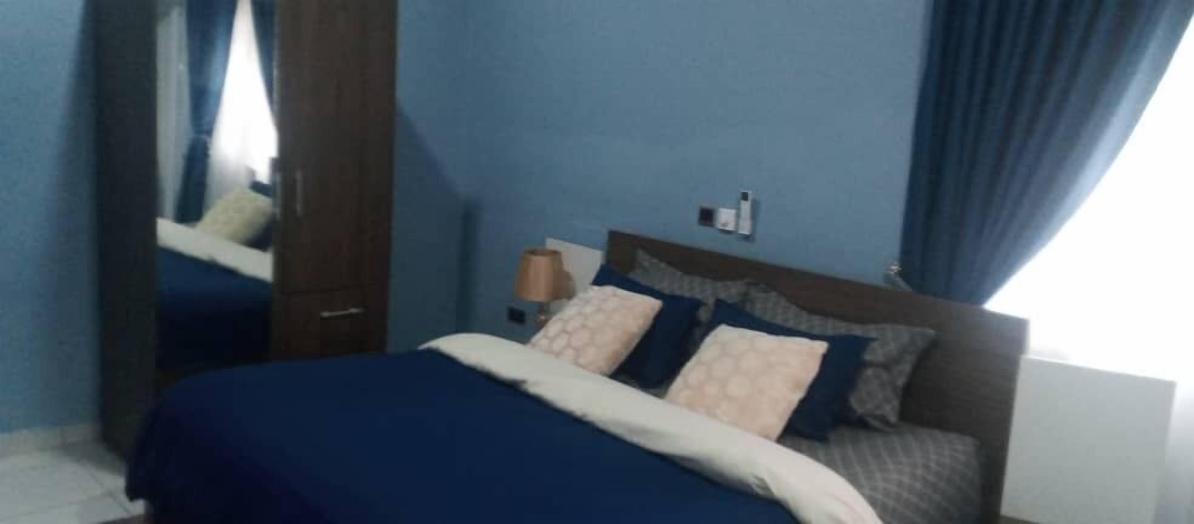 Une chambre à coucher comprenant un lit, une table de chevet, un miroir et un luminaire fixé au mur.