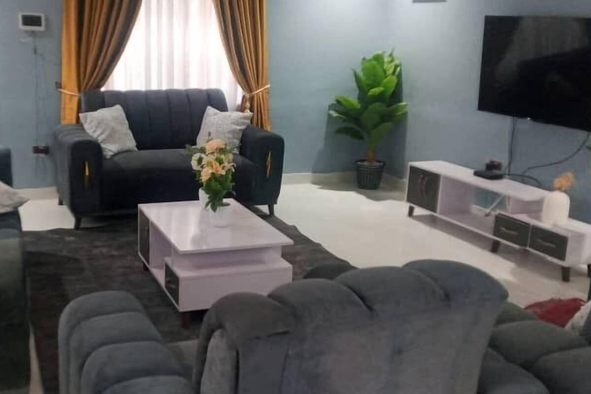 A living room with a dark-colored sofa set, a white coffee table, and a flat-screen TV mounted on the wall.