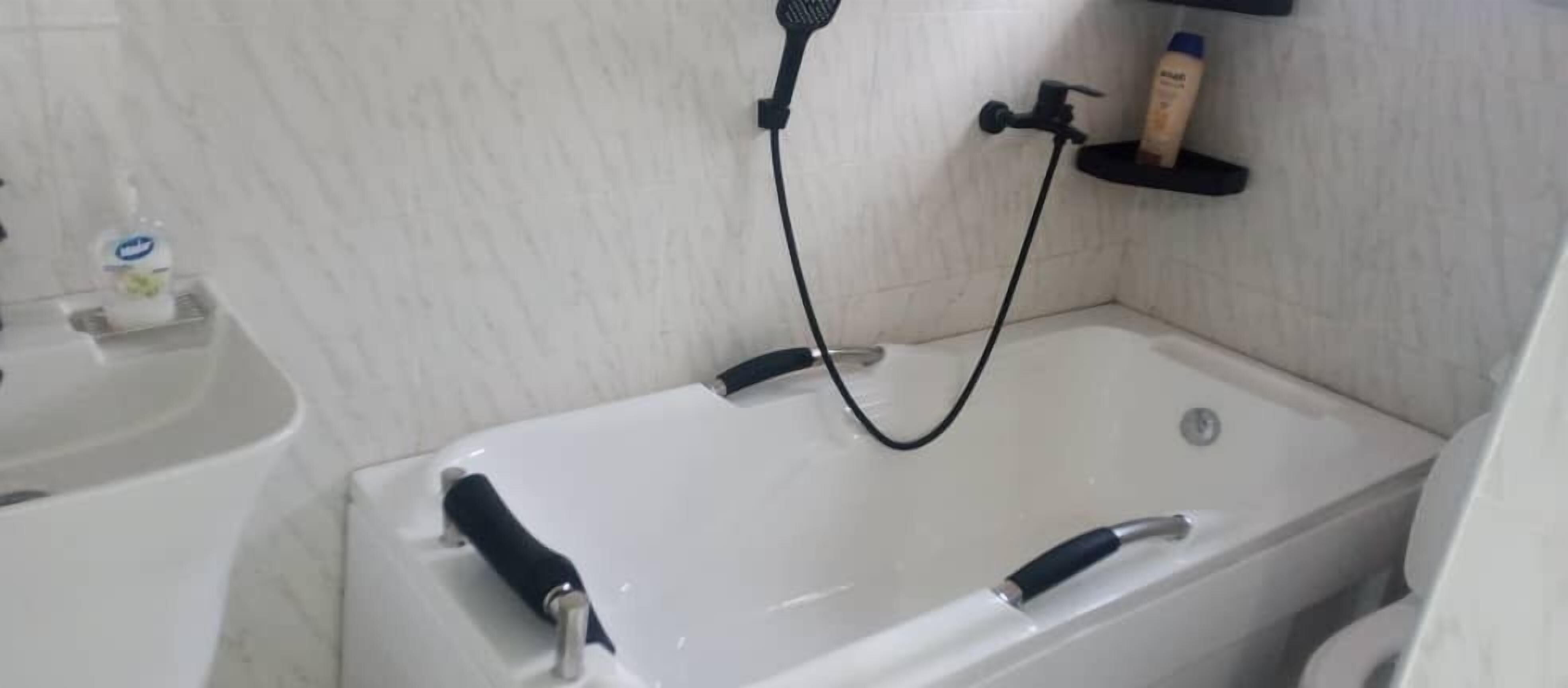 Een badkamer met een witte badkuip, een handdouche en een klein plankje met toiletartikelen.