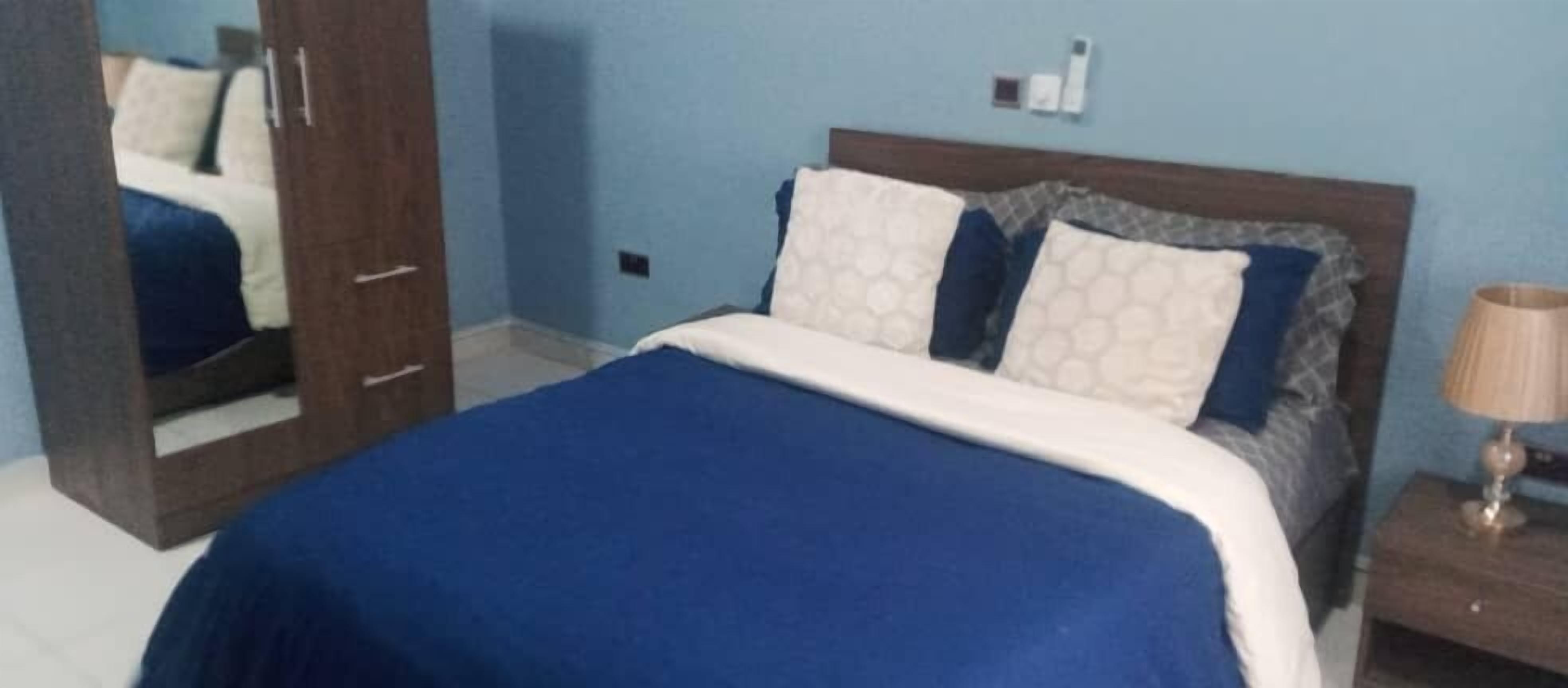 A bedroom with a bed, a nightstand, a lamp, and a mirror.