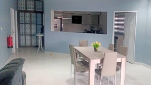 A modern dining area with a wooden table and chairs, a small potted plant, and a kitchen in the background. - SNS Apartments (Adentan)